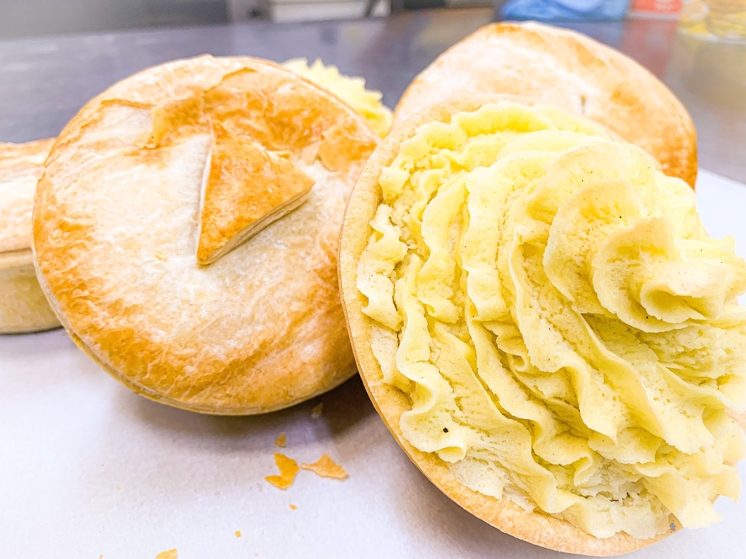 Golden pies fresh on the bench, one topped with piped mash